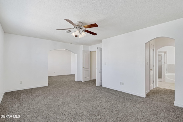 carpeted spare room featuring arched walkways, baseboards, a textured ceiling, and a ceiling fan