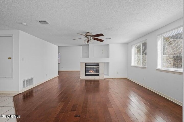 unfurnished living room featuring visible vents, hardwood / wood-style flooring, baseboards, ceiling fan, and a tile fireplace