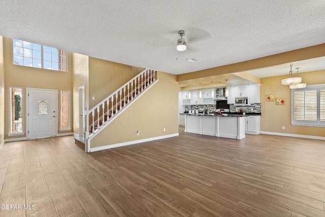 kitchen with dark countertops, stainless steel microwave, wall chimney range hood, open floor plan, and white cabinets