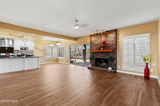 unfurnished living room featuring visible vents, a stone fireplace, a textured ceiling, a ceiling fan, and dark wood-style flooring