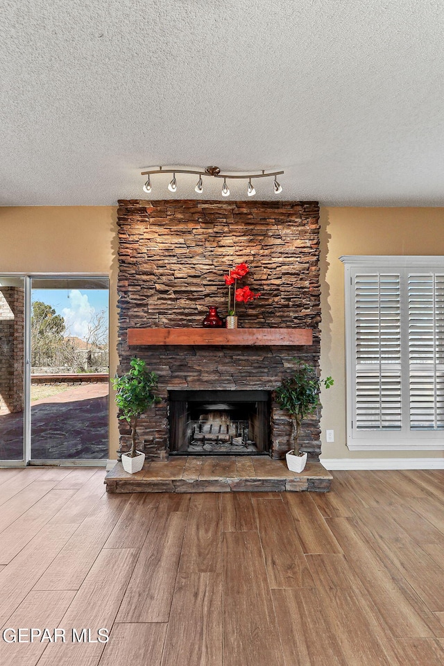 unfurnished living room with a stone fireplace, a textured ceiling, baseboards, and wood finished floors