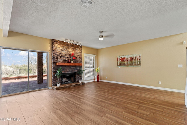 unfurnished living room with a stone fireplace, wood finished floors, a ceiling fan, and visible vents