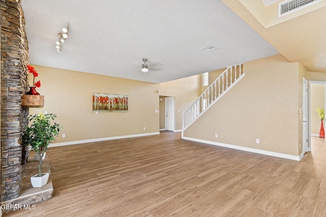 unfurnished living room with wood finished floors, baseboards, visible vents, ceiling fan, and a textured ceiling