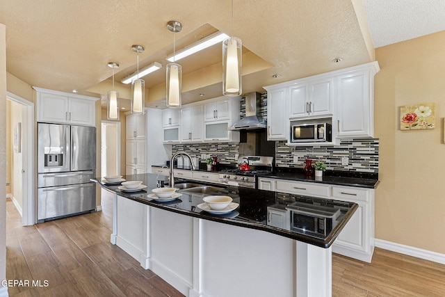 kitchen with dark countertops, stainless steel appliances, light wood-type flooring, and wall chimney range hood