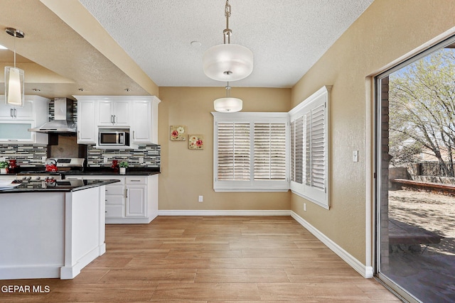 kitchen featuring tasteful backsplash, dark countertops, white cabinetry, appliances with stainless steel finishes, and wall chimney range hood