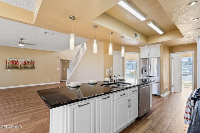 kitchen featuring wood finished floors, visible vents, a tray ceiling, a sink, and appliances with stainless steel finishes