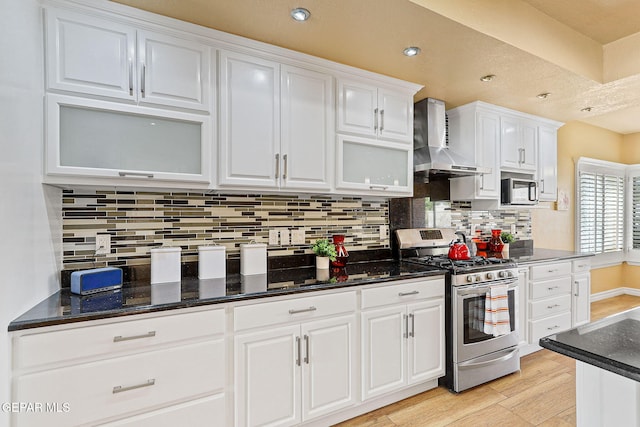 kitchen featuring wall chimney range hood, tasteful backsplash, stainless steel range with gas cooktop, white cabinets, and light wood finished floors