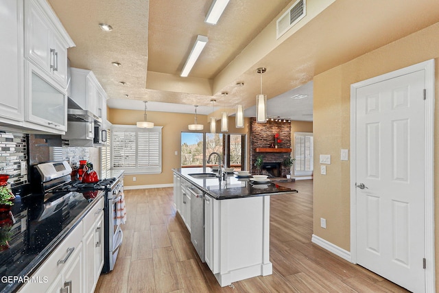 kitchen with visible vents, a sink, a stone fireplace, appliances with stainless steel finishes, and a raised ceiling