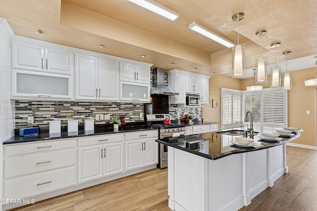 kitchen with light wood-type flooring, a sink, white cabinetry, stainless steel appliances, and wall chimney range hood