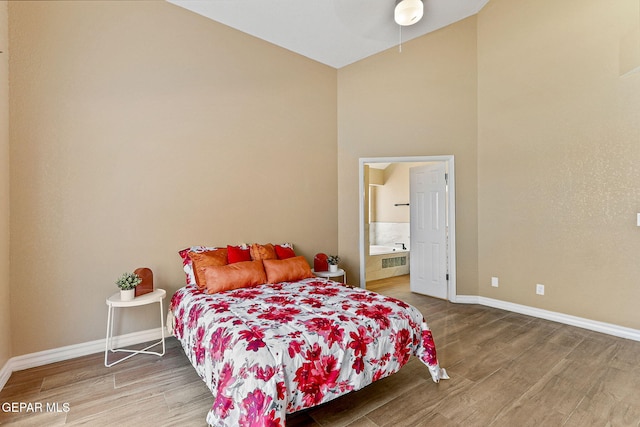 bedroom with ensuite bath, wood finished floors, baseboards, and high vaulted ceiling