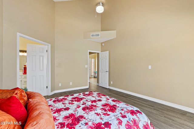 bedroom with visible vents, a high ceiling, baseboards, and wood finished floors