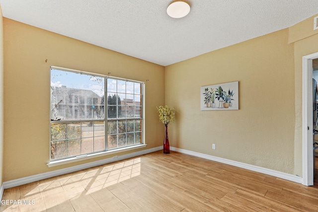 empty room with baseboards, a textured ceiling, and wood finished floors