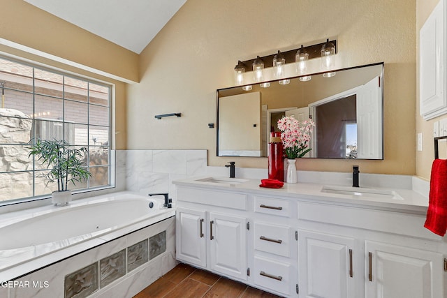 full bath featuring a sink, lofted ceiling, a jetted tub, and wood finish floors