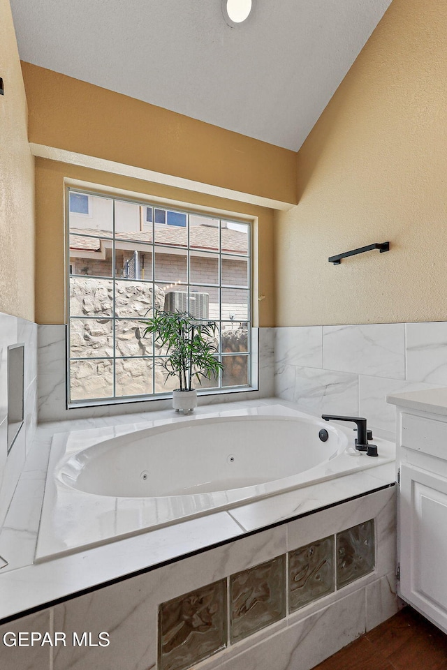 bathroom featuring lofted ceiling, a tub with jets, vanity, and a textured wall