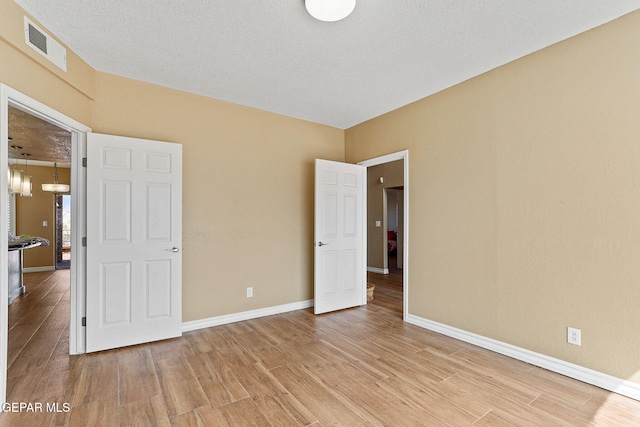 unfurnished bedroom featuring visible vents, baseboards, a textured ceiling, and light wood-style flooring