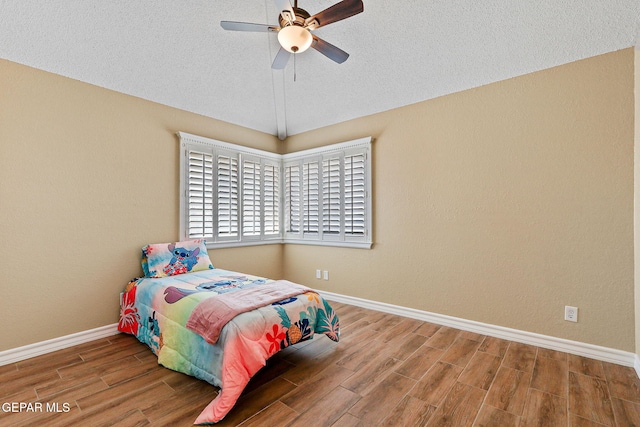 bedroom with wood finished floors, baseboards, lofted ceiling, ceiling fan, and a textured ceiling