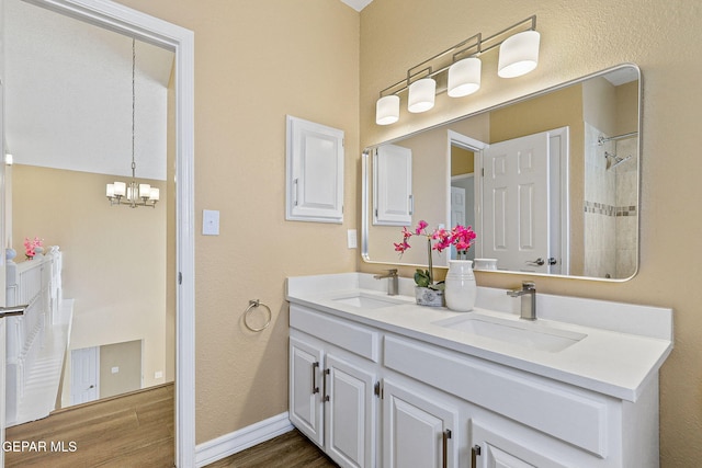 full bathroom featuring double vanity, wood finished floors, an inviting chandelier, and a sink