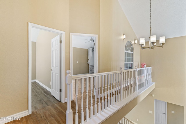 hallway with a chandelier, baseboards, high vaulted ceiling, and wood finished floors