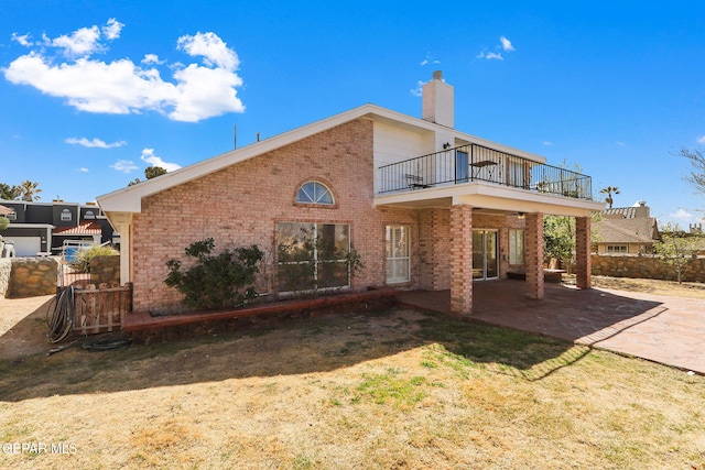 back of property with a patio, a balcony, fence, a chimney, and brick siding