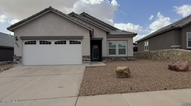 view of front facade with a tiled roof, stucco siding, driveway, stone siding, and an attached garage