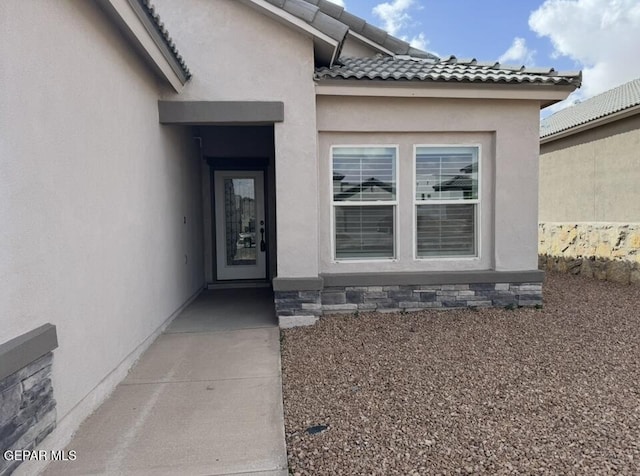 view of exterior entry with a tiled roof and stucco siding