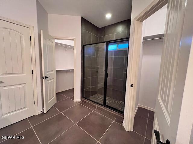 full bathroom featuring tile patterned floors, a stall shower, a walk in closet, and baseboards