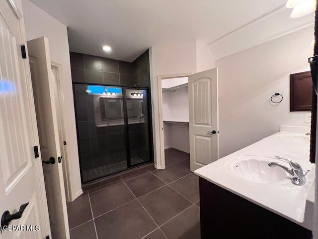 full bathroom with a walk in closet, a stall shower, a sink, tile patterned flooring, and double vanity