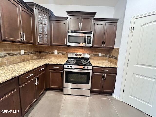 kitchen with dark brown cabinets, light stone countertops, backsplash, and appliances with stainless steel finishes