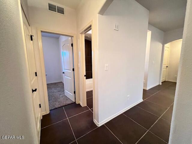 hallway featuring tile patterned floors, arched walkways, visible vents, and baseboards