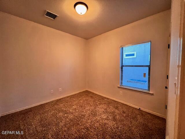 unfurnished room featuring dark colored carpet, visible vents, and baseboards