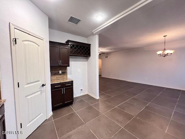 kitchen featuring visible vents, light stone countertops, dark brown cabinetry, decorative backsplash, and dark tile patterned flooring