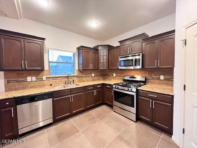 kitchen with a sink, light stone counters, dark brown cabinets, and stainless steel appliances