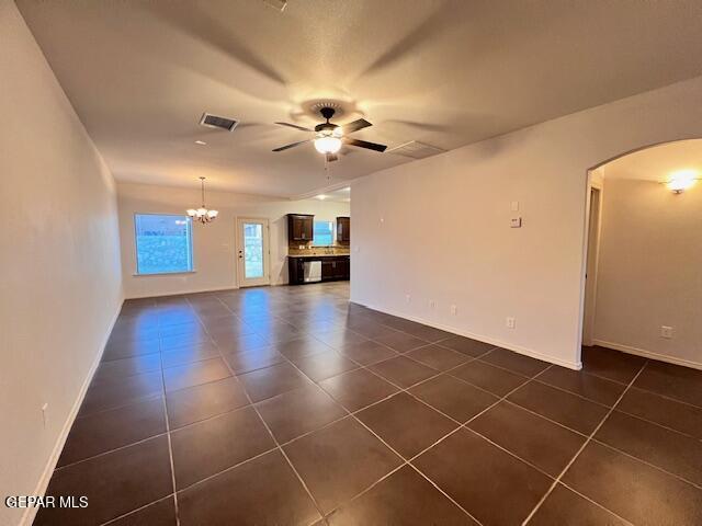 unfurnished living room with arched walkways, visible vents, ceiling fan with notable chandelier, and dark tile patterned floors