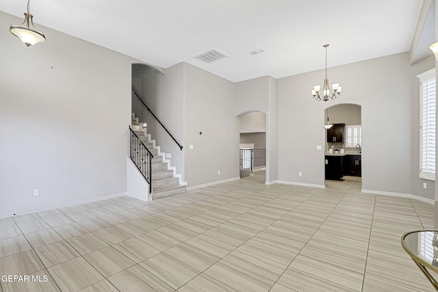 unfurnished living room featuring visible vents, baseboards, stairs, arched walkways, and a notable chandelier