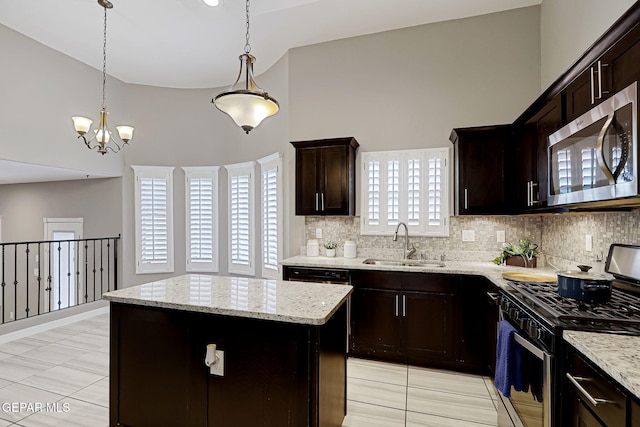 kitchen with light stone countertops, a kitchen island, a sink, stainless steel appliances, and backsplash