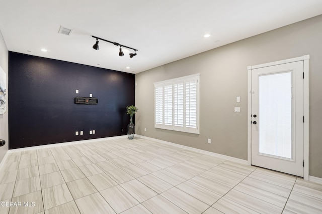 interior space featuring visible vents, rail lighting, an accent wall, and baseboards