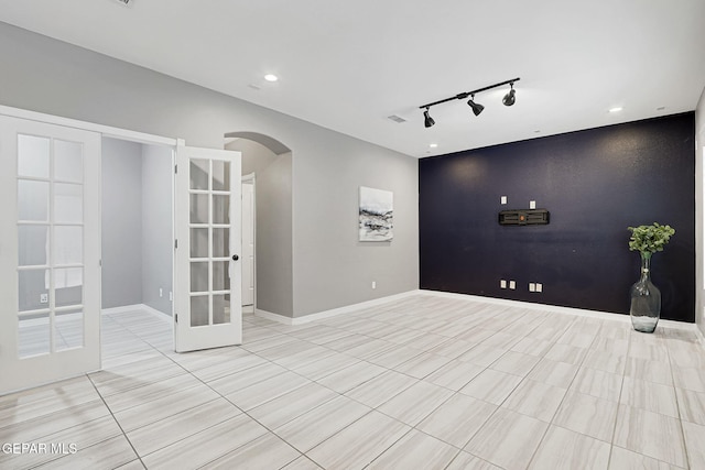 empty room featuring visible vents, baseboards, arched walkways, french doors, and an accent wall