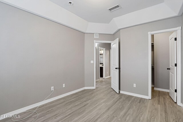 unfurnished bedroom with visible vents, baseboards, a walk in closet, and light wood-style flooring