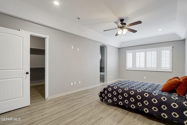 bedroom featuring a walk in closet, wood finished floors, recessed lighting, arched walkways, and baseboards