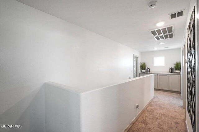 hallway with an upstairs landing, visible vents, and light colored carpet
