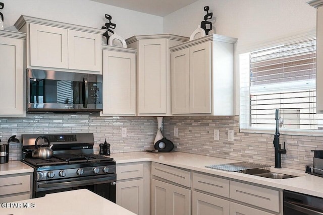 kitchen featuring light countertops, backsplash, appliances with stainless steel finishes, and a sink