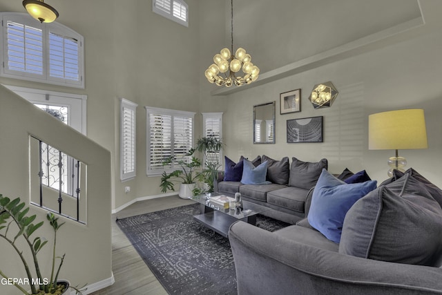 living area with a chandelier, baseboards, a towering ceiling, and wood finished floors