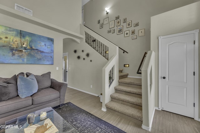 living room featuring visible vents, wood finished floors, a high ceiling, baseboards, and stairs