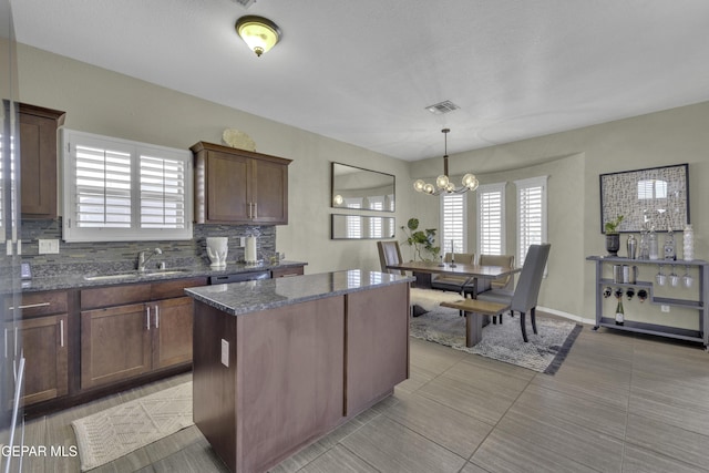 kitchen featuring tasteful backsplash, visible vents, a center island, a chandelier, and a sink