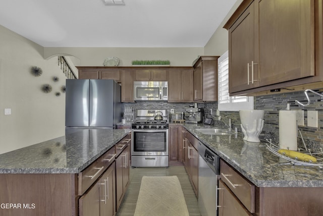 kitchen featuring dark stone counters, tasteful backsplash, appliances with stainless steel finishes, and a sink