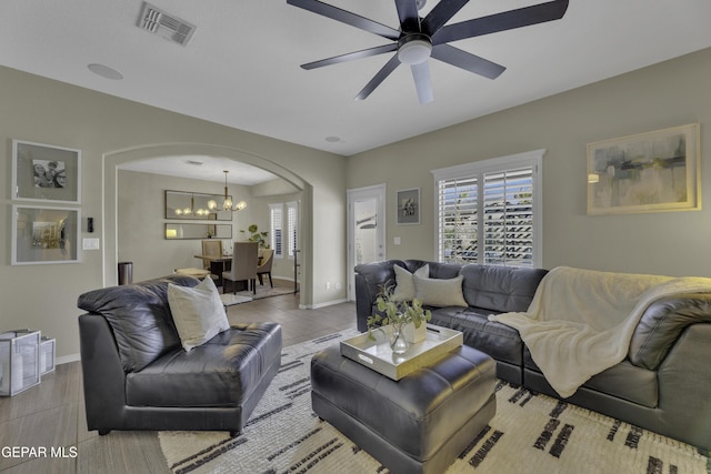 living area with visible vents, tile patterned floors, baseboards, ceiling fan with notable chandelier, and arched walkways