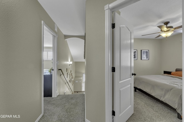 hall featuring an upstairs landing, carpet, and a textured wall