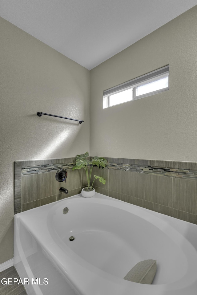 bathroom with a garden tub and a textured wall