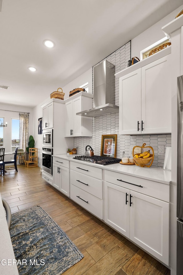 7402 Wooden Nickel Dr, El Paso, TX 79911 - kitchen featuring wall chimney exhaust hood, light wood-type flooring, stainless steel appliances, white cabinets, and decorative backsplash