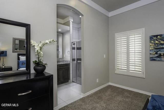 bedroom featuring baseboards, light carpet, ensuite bathroom, light tile patterned flooring, and arched walkways